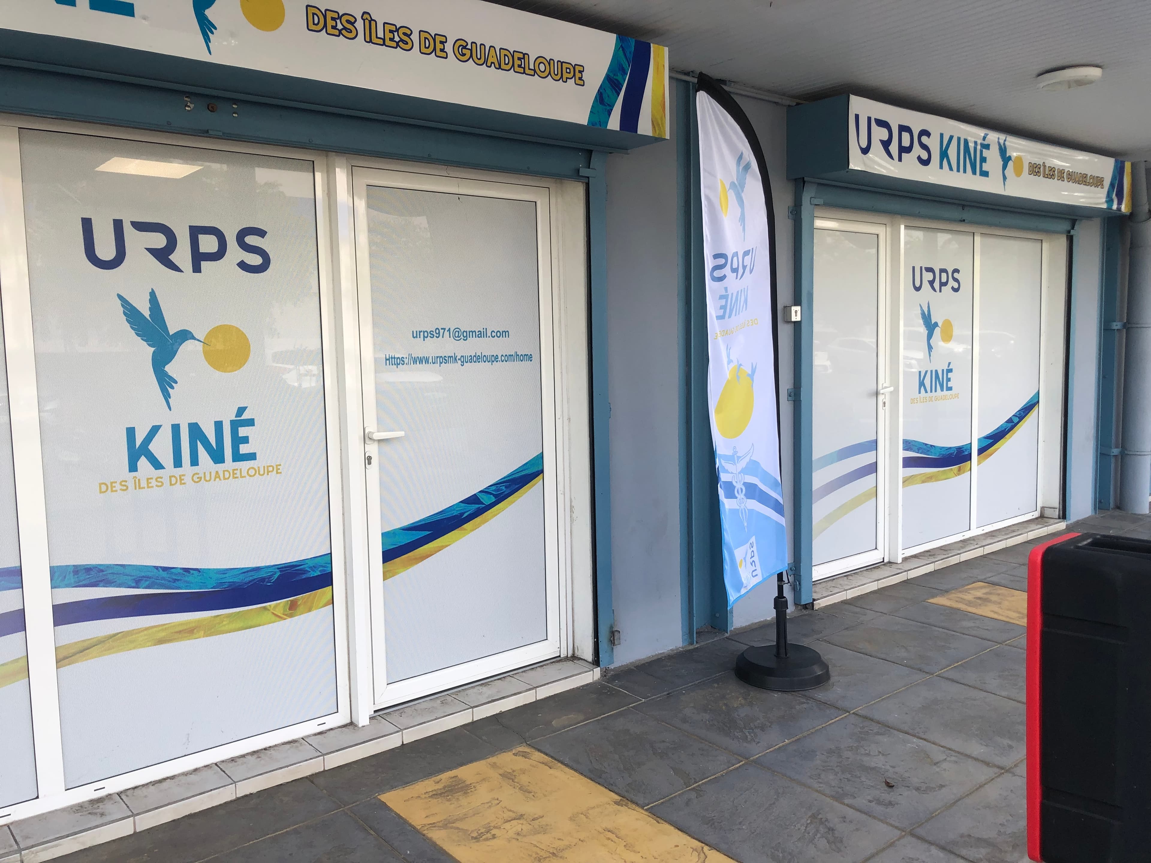 La façade des locaux de l'URPS Kiné, vitrines au logo du colibri et oriflamme devant l'entrée